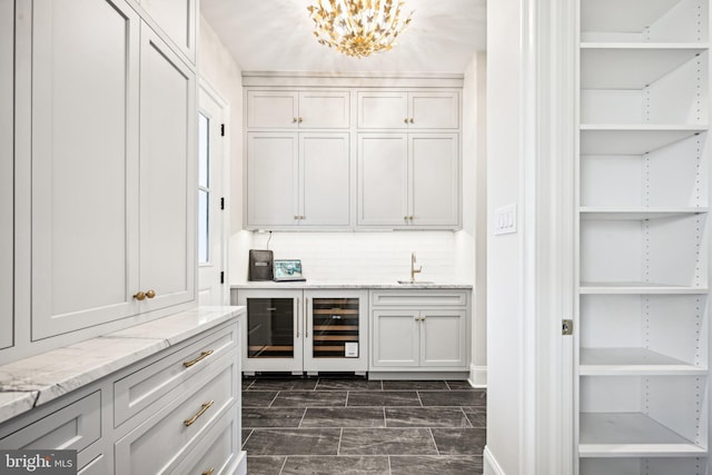 bar with white cabinets, wine cooler, sink, backsplash, and light stone counters