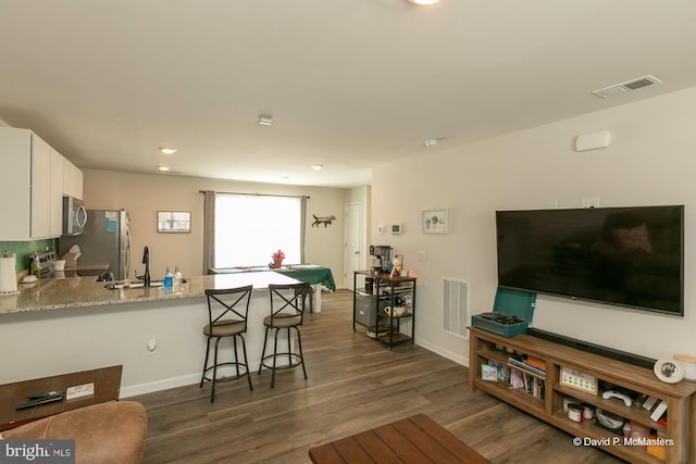 kitchen with appliances with stainless steel finishes, white cabinets, kitchen peninsula, a breakfast bar, and light stone counters