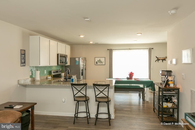 kitchen with appliances with stainless steel finishes, tasteful backsplash, white cabinets, kitchen peninsula, and dark wood-type flooring