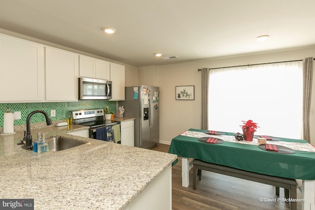 kitchen with tasteful backsplash, white cabinetry, sink, stainless steel appliances, and light stone counters