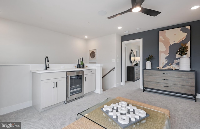 kitchen featuring sink, white cabinets, beverage cooler, ceiling fan, and light carpet