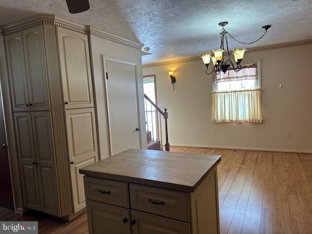 kitchen with a chandelier, a textured ceiling, ornamental molding, a kitchen island, and hardwood / wood-style flooring