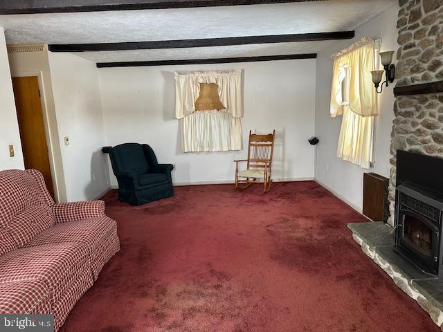 sitting room with a stone fireplace, carpet floors, a textured ceiling, and beam ceiling