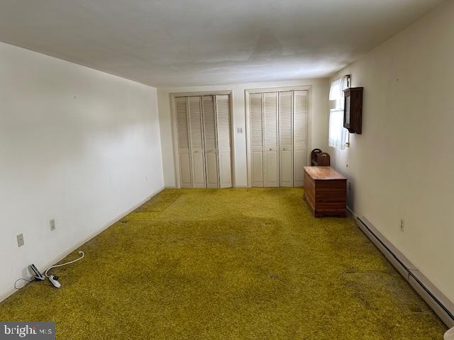 unfurnished bedroom featuring a baseboard radiator, carpet, and two closets