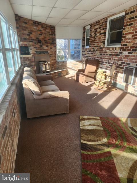 carpeted living room with brick wall, a wood stove, and a paneled ceiling