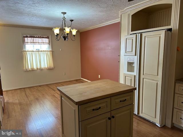 kitchen with crown molding, a center island, a textured ceiling, decorative light fixtures, and light wood-type flooring