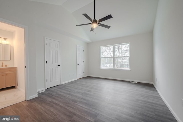 unfurnished bedroom featuring two closets, ceiling fan, ensuite bath, dark wood-type flooring, and vaulted ceiling