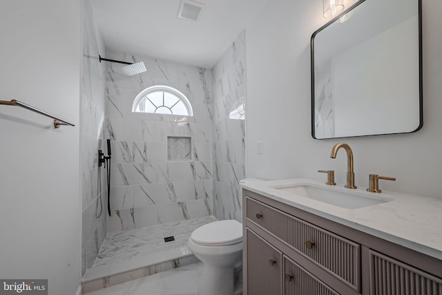 bathroom featuring toilet, a tile shower, and vanity