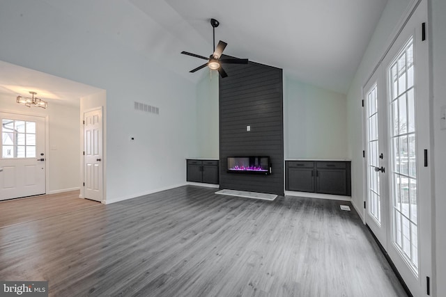 unfurnished living room with hardwood / wood-style flooring, a large fireplace, ceiling fan with notable chandelier, and plenty of natural light