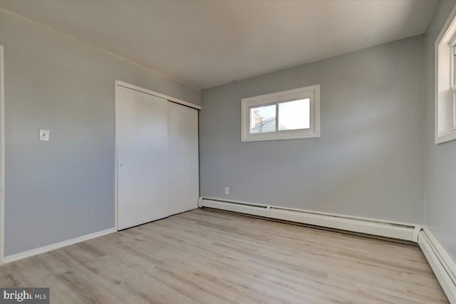 unfurnished bedroom featuring a baseboard radiator, light hardwood / wood-style floors, and a closet