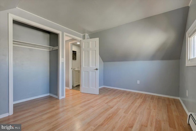 unfurnished bedroom with lofted ceiling, a baseboard radiator, a closet, and light wood-type flooring