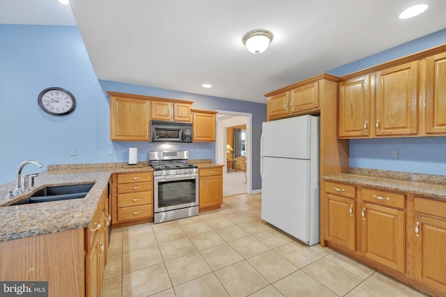 kitchen with stainless steel gas range, white fridge, sink, light stone counters, and light tile patterned floors