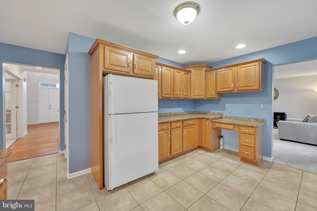 kitchen featuring light tile patterned floors, light stone counters, and white fridge