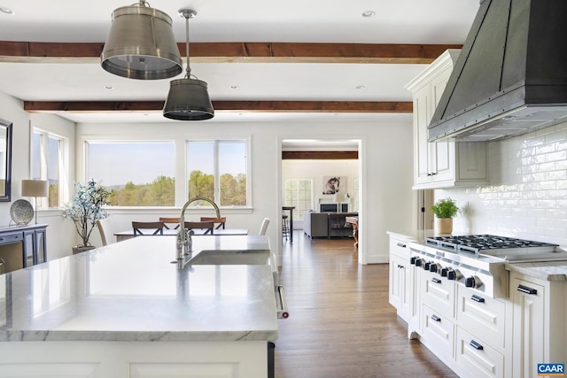 kitchen with stainless steel gas cooktop, custom range hood, sink, decorative light fixtures, and backsplash