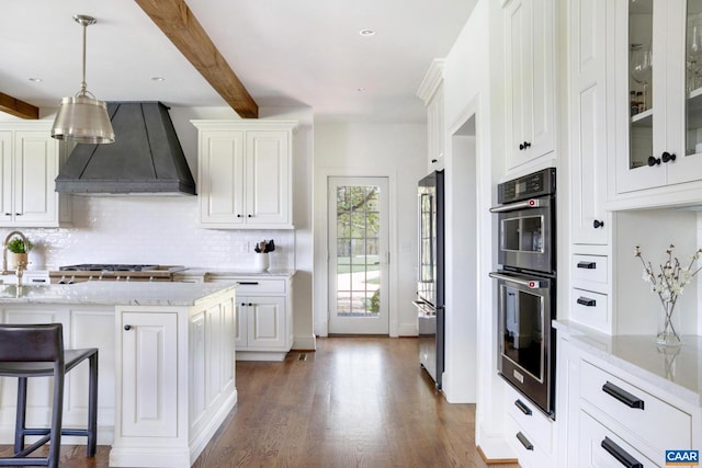 kitchen featuring beamed ceiling, custom range hood, white cabinets, stainless steel appliances, and light stone counters