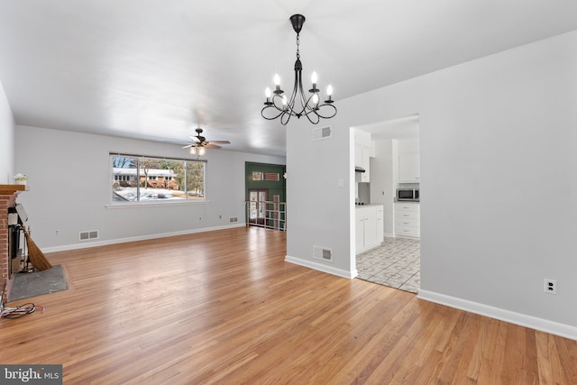 unfurnished living room featuring a brick fireplace, ceiling fan with notable chandelier, and light wood-type flooring