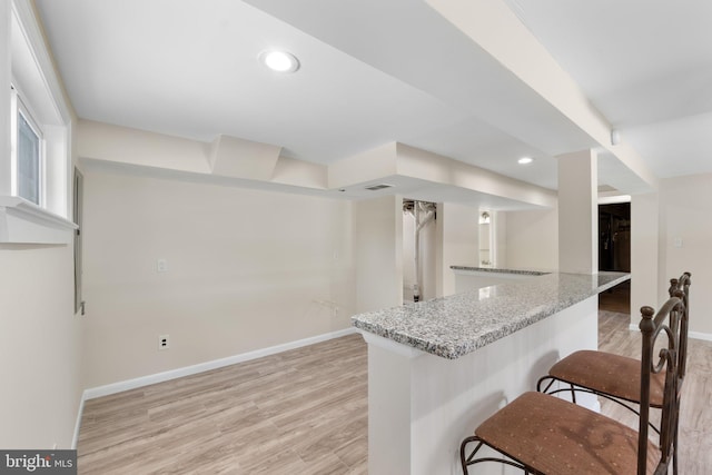 kitchen with light stone counters, a breakfast bar, light hardwood / wood-style flooring, and kitchen peninsula