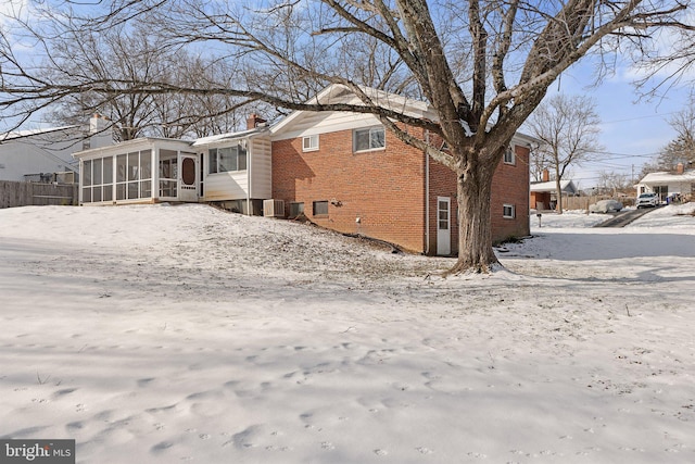 snow covered rear of property featuring a sunroom