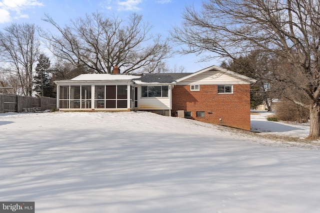 snow covered rear of property featuring a sunroom