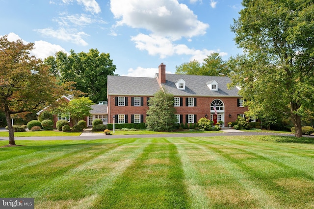 colonial-style house featuring a chimney and a front lawn