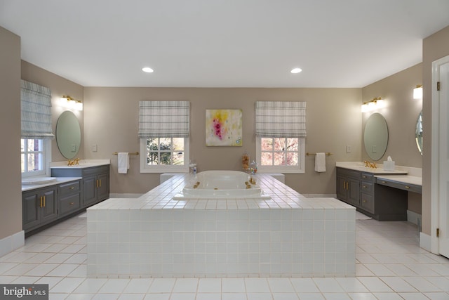 bathroom featuring two vanities, a tub with jets, a wealth of natural light, and a sink