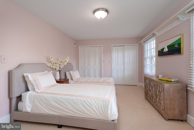 bedroom featuring visible vents, light colored carpet, baseboards, and two closets