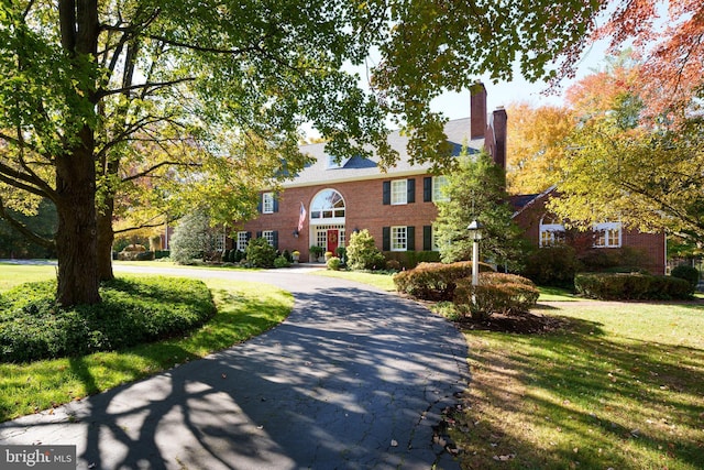 view of front of house featuring brick siding, driveway, a chimney, and a front yard