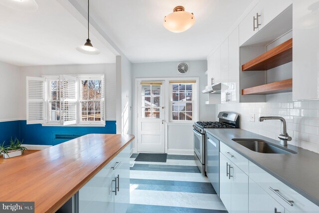 kitchen with butcher block countertops, decorative light fixtures, sink, white cabinets, and stainless steel gas range