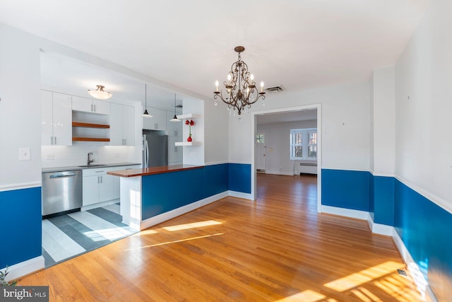 kitchen with appliances with stainless steel finishes, white cabinetry, wood-type flooring, sink, and hanging light fixtures