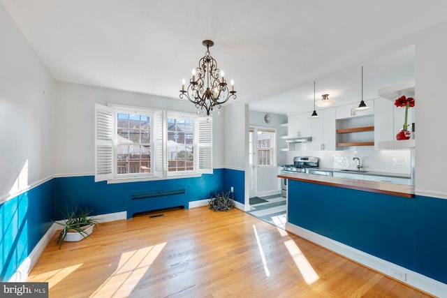 kitchen featuring stainless steel gas stove, hanging light fixtures, backsplash, light hardwood / wood-style floors, and white cabinets