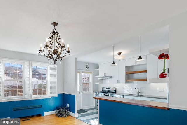 kitchen featuring appliances with stainless steel finishes, radiator, pendant lighting, white cabinetry, and sink