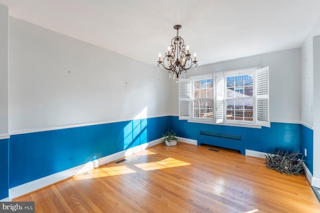 unfurnished room with hardwood / wood-style flooring, radiator heating unit, and a chandelier