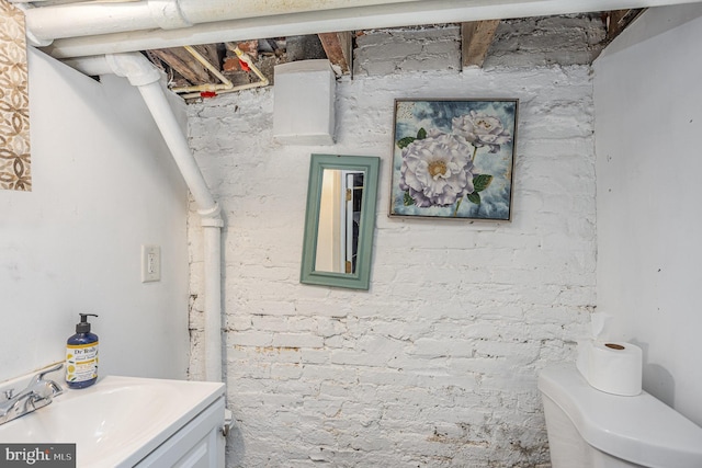 bathroom featuring brick wall, toilet, and vanity