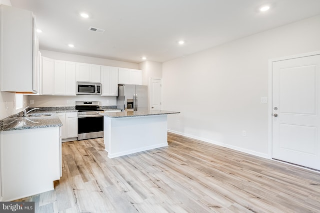 kitchen featuring a center island, white cabinetry, stainless steel appliances, dark stone countertops, and light hardwood / wood-style floors