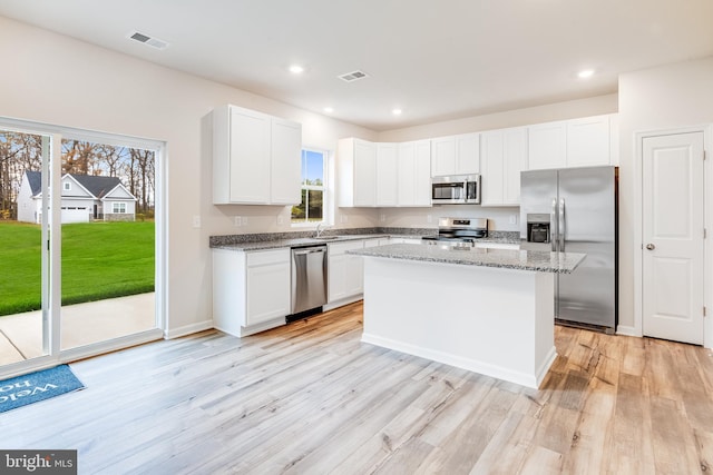 kitchen featuring white cabinetry, stainless steel appliances, a center island, light stone counters, and sink