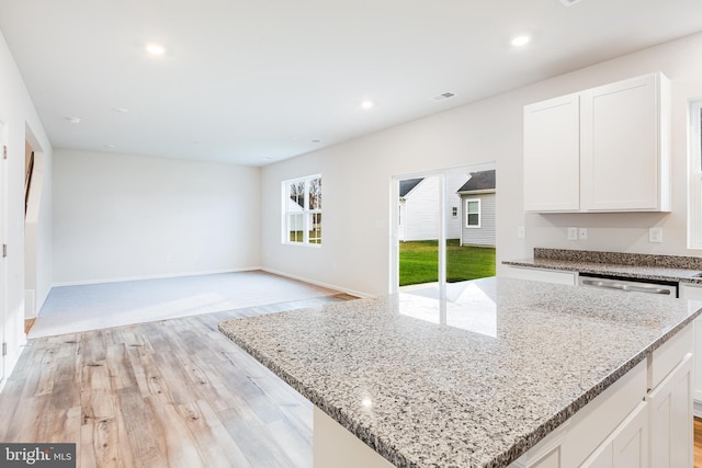 kitchen with light wood-type flooring, white cabinetry, light stone counters, and a kitchen island