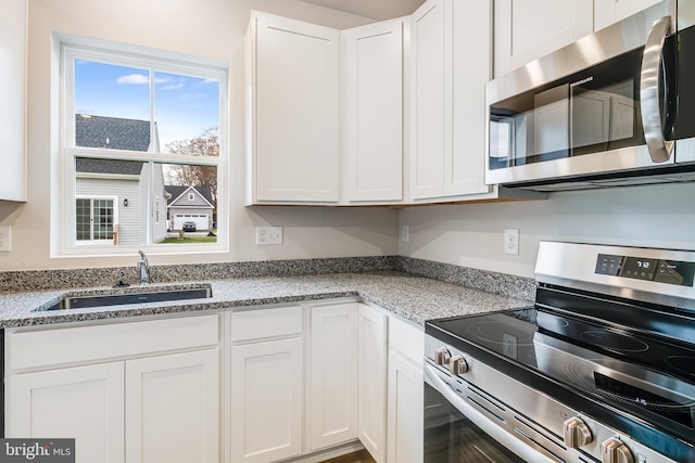 kitchen with sink, light stone counters, stainless steel appliances, and white cabinetry