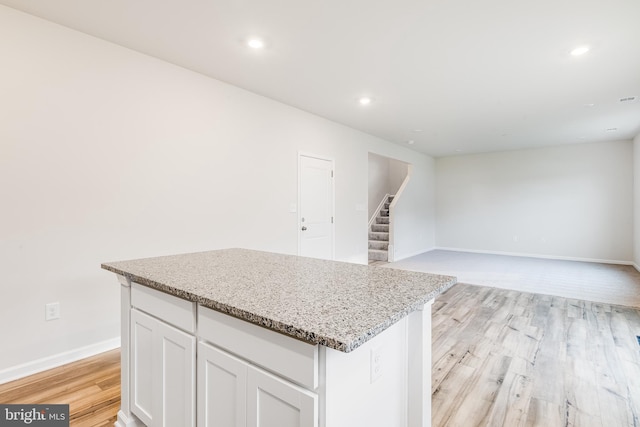 kitchen with light stone counters, white cabinets, a center island, and light hardwood / wood-style flooring