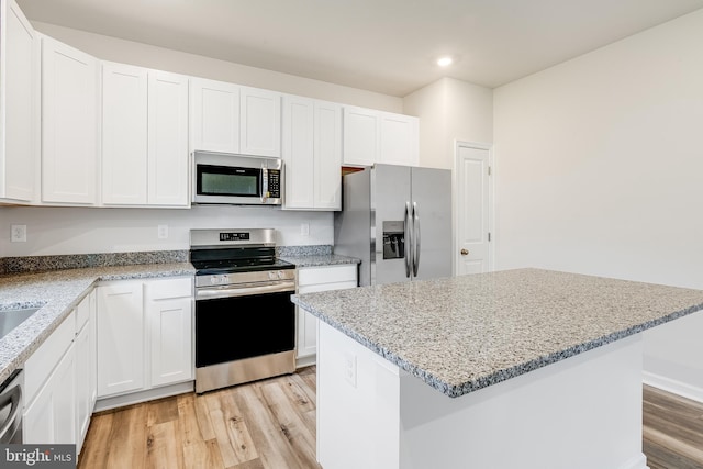 kitchen with white cabinets, appliances with stainless steel finishes, a center island, light hardwood / wood-style floors, and light stone counters