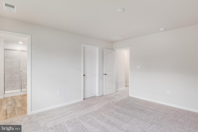 unfurnished bedroom featuring light carpet and connected bathroom