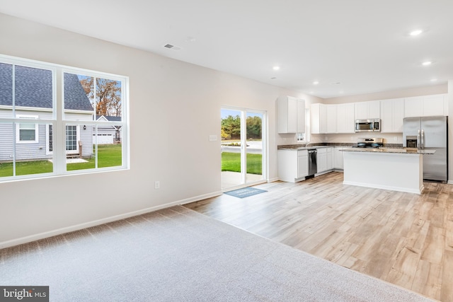 kitchen with white cabinets, a kitchen island, stainless steel appliances, dark stone countertops, and light hardwood / wood-style flooring