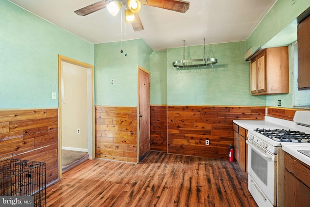 kitchen with ceiling fan, gas range gas stove, dark hardwood / wood-style flooring, and wooden walls