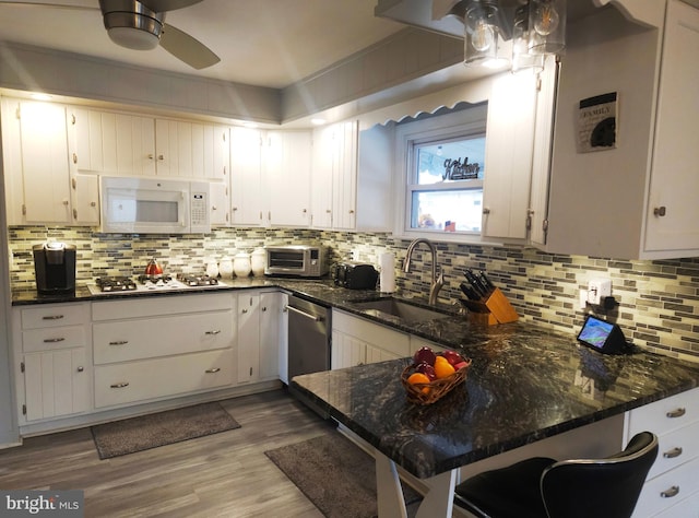 kitchen with kitchen peninsula, sink, white cabinetry, gas stovetop, and dark stone counters