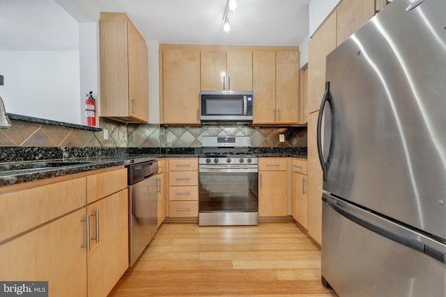 kitchen with light hardwood / wood-style floors, appliances with stainless steel finishes, tasteful backsplash, light brown cabinetry, and dark stone counters