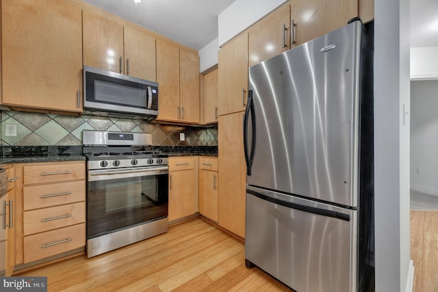 kitchen with appliances with stainless steel finishes, dark stone countertops, decorative backsplash, light brown cabinetry, and light hardwood / wood-style flooring