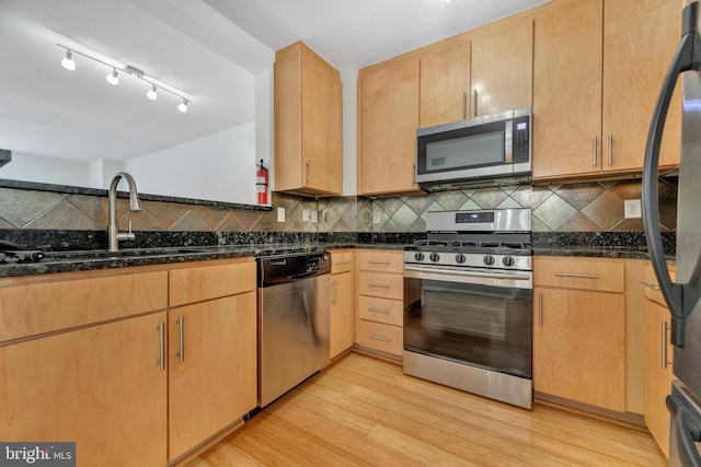 kitchen featuring appliances with stainless steel finishes, light wood-type flooring, light brown cabinetry, dark stone counters, and sink