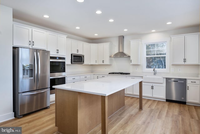 kitchen with wall chimney exhaust hood, white cabinetry, stainless steel appliances, and sink