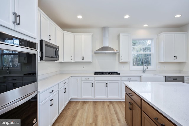 kitchen featuring wall chimney range hood, sink, white cabinets, and appliances with stainless steel finishes