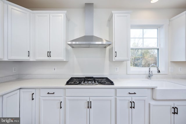 kitchen with white cabinets, stainless steel gas stovetop, sink, and wall chimney range hood