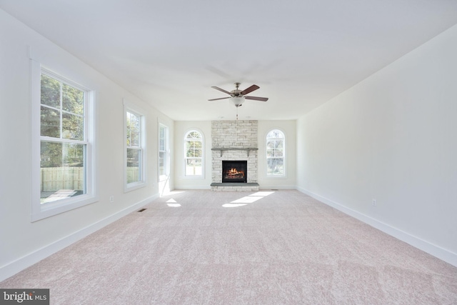 unfurnished living room with light carpet, a stone fireplace, and ceiling fan